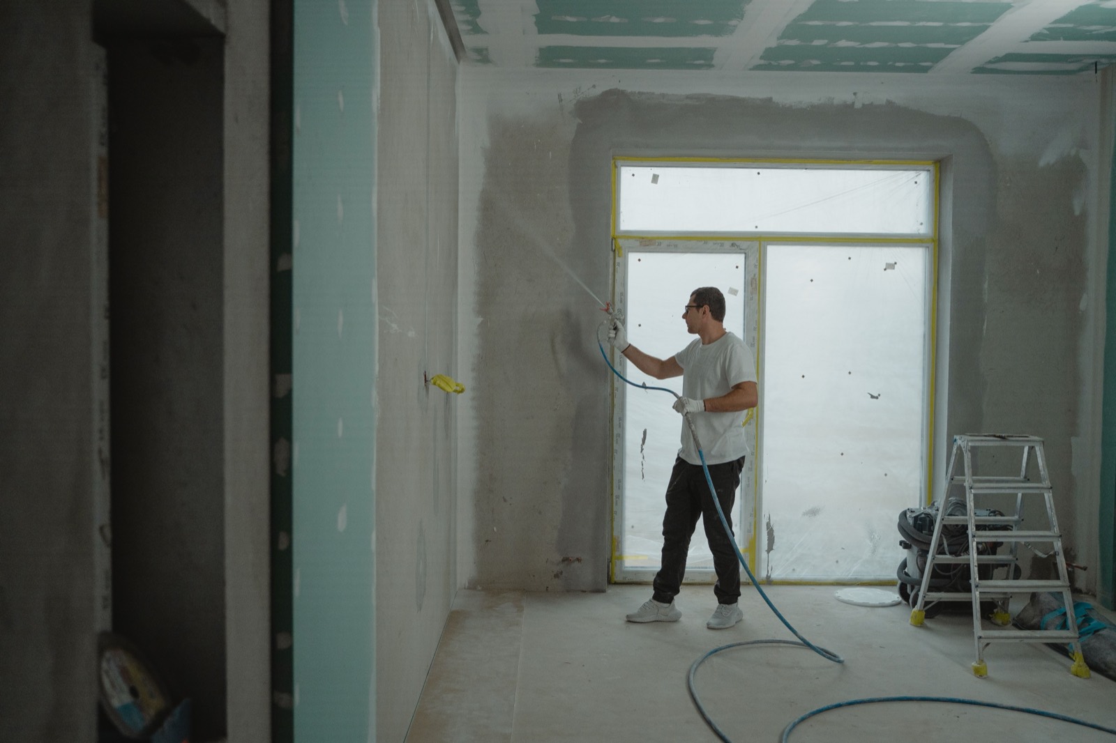 A painter spraying an interior wall with an airless gun, both hands on the tool